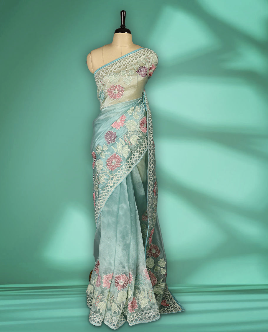 Aqua Blue colour organza designer saree featuring delicate pastel floral embroidery in pink, mint green, and white across the body, with a scalloped border accentuated by floral threadwork, and a gracefully embroidered pallu paired with matching blouse.