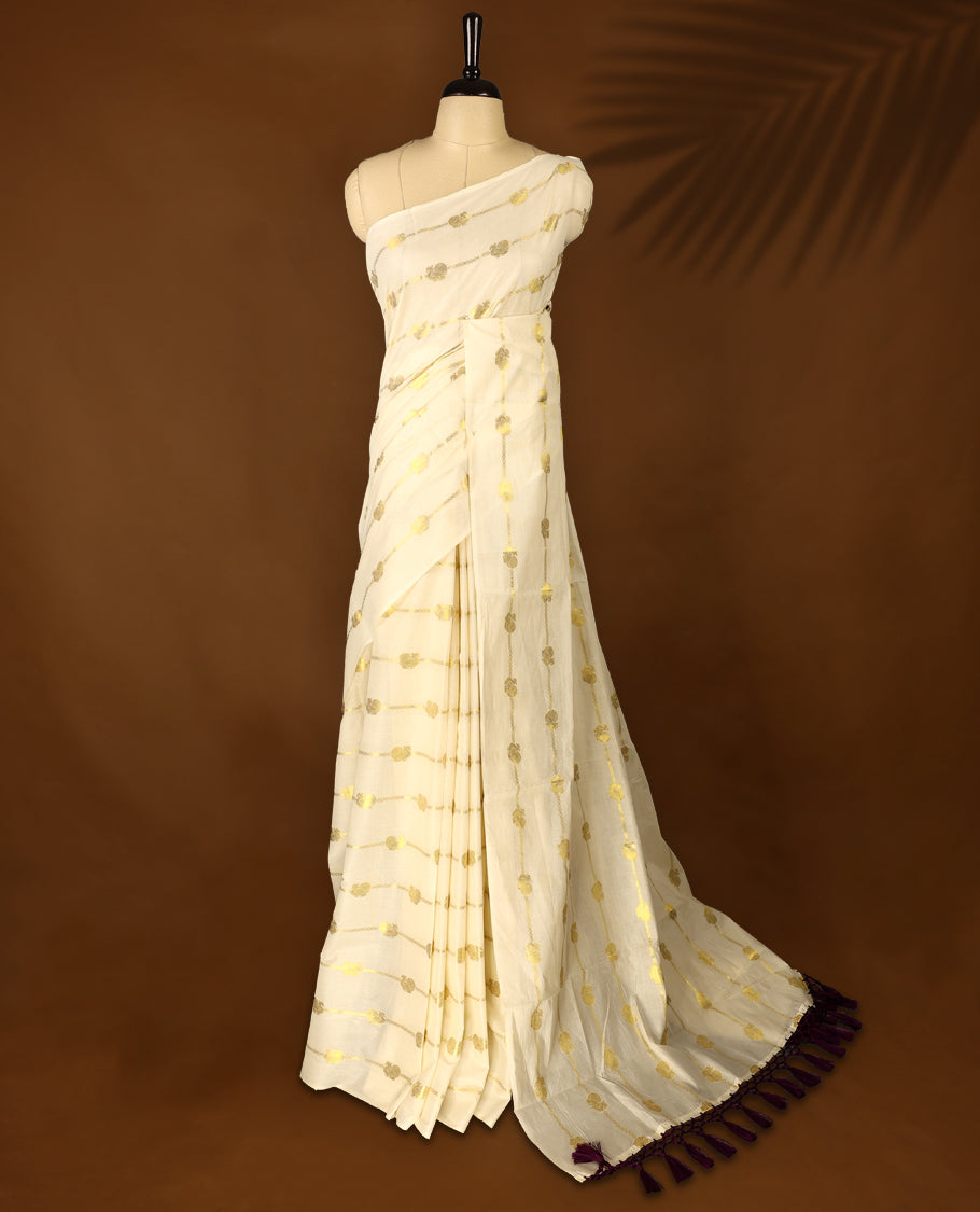 Elegant off white colour cotton Kerala saree featuring a gold Zari stripes with peacock motifs on body, with purple colour tassels offering a classic and graceful look, paired with a matching blouse.