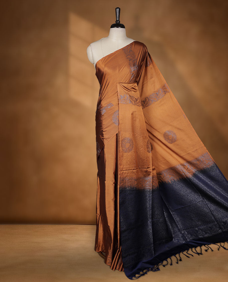 Mustard colour semi soft silk saree adorned with delicate woven floral kodi motifs on the body, complemented by a contrast navy blue colour woven pallu with intricate detailing and tassel accents without border & Comes with a matching blouse piece.