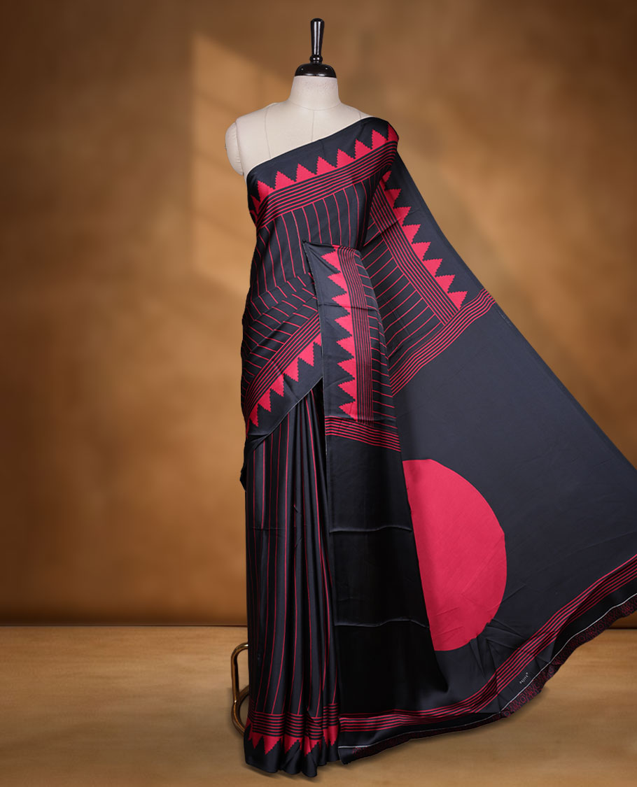 Black colour semi modal saree highlighted with red triangle border accents and sleek striped detailing across the drape, featuring a bold oversized red circular motif on the pallu, paired with a matching printed blouse.