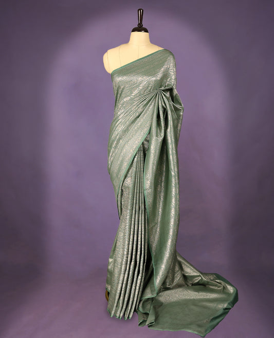 Pastel green colour semi Banaras Katan saree featuring an antique silver zari jacquard body, complemented by a self colour traditional border with a floral kodi design, paired with a matching blouse
