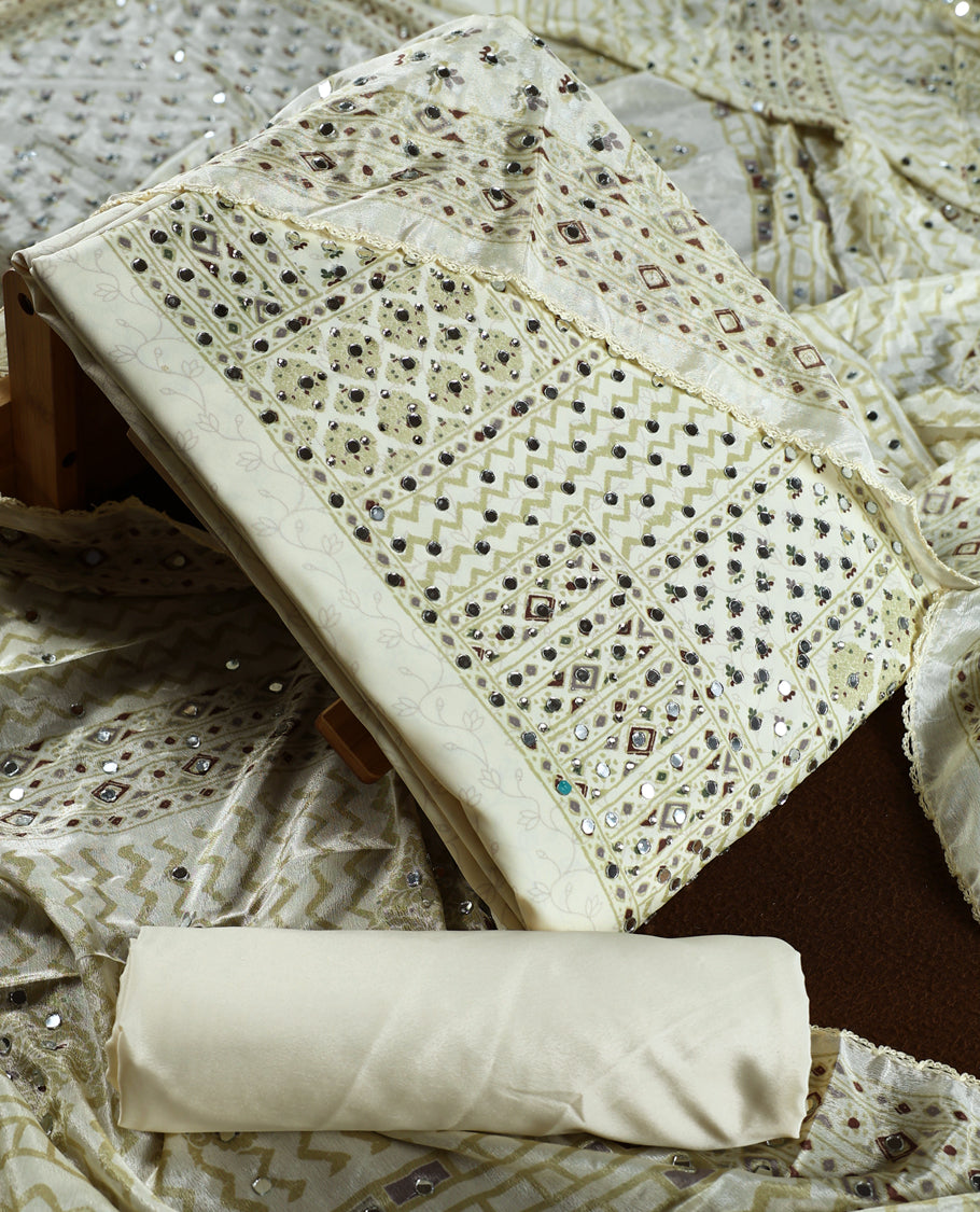 Cream colour churidar material adorned with intricate geometric designs and sparkling mirror work, paired with a plain matching bottom and dupatta.