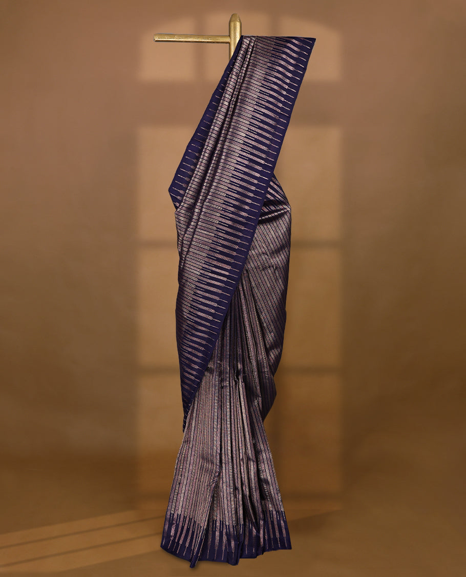 Ink purple colour Kancheepuram designer saree adorned with distinctive vertical zari lines featuring intricate arrowhead and herringbone motifs on the body, designed without a border, and paired with a matching blouse.