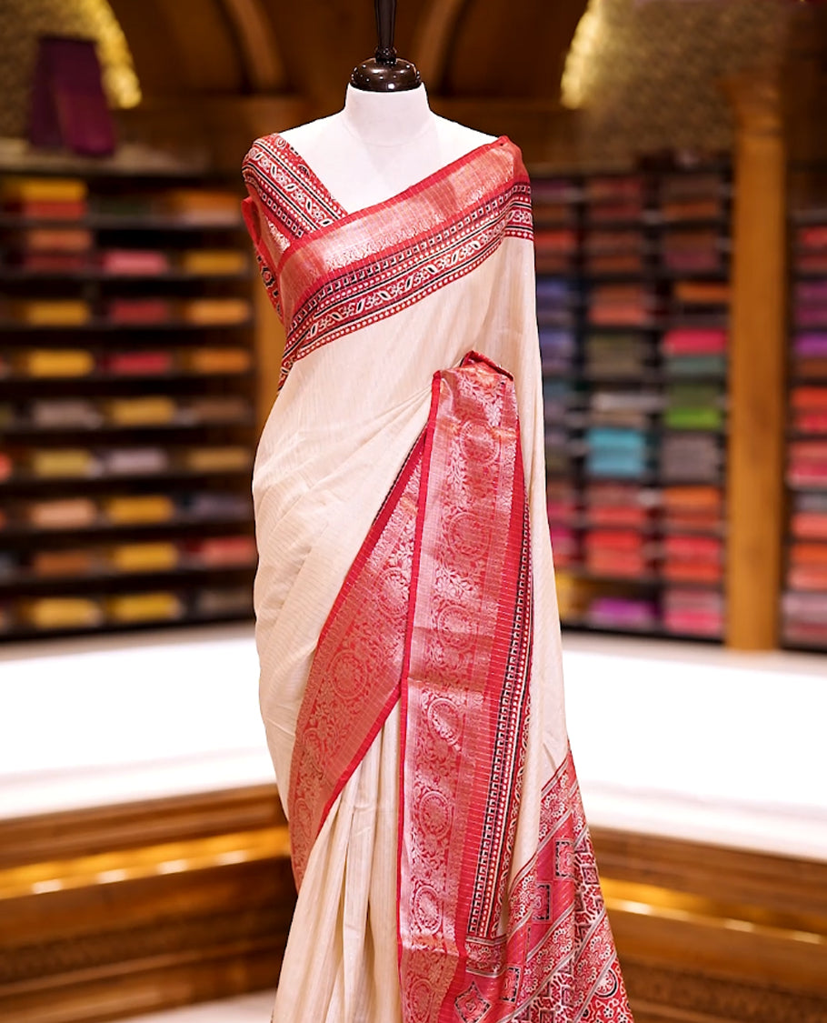 Beige Dolla silk saree featuring antique zari stripes across the body, adorned with a striking Ajrak and Traditional red colour border, ajrak printed pallu and paired with a perfectly matching blouse.