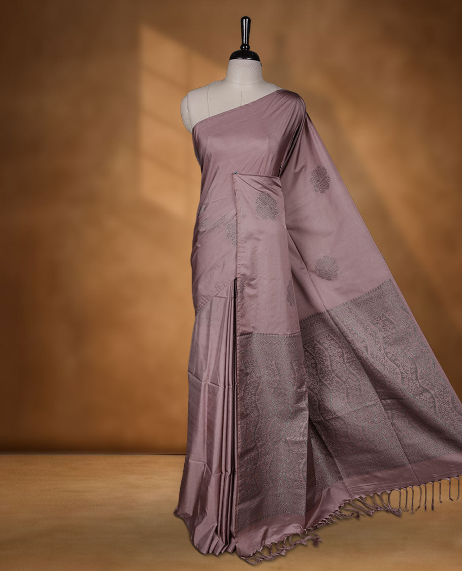 Pinkish beige colour semi soft silk saree adorned with delicate woven floral motifs on the body, complemented by a Self colour woven pallu with intricate detailing and tassel accents without border & Comes with a matching blouse piece.