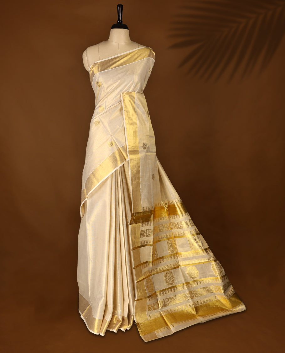 Elegant off white colour tissue Kerala saree with gold zari buttas, broad kasavu border, and richly woven traditional pallu. Crafted in cotton and paired with a matching blouse, perfect for festive and traditional occasions.