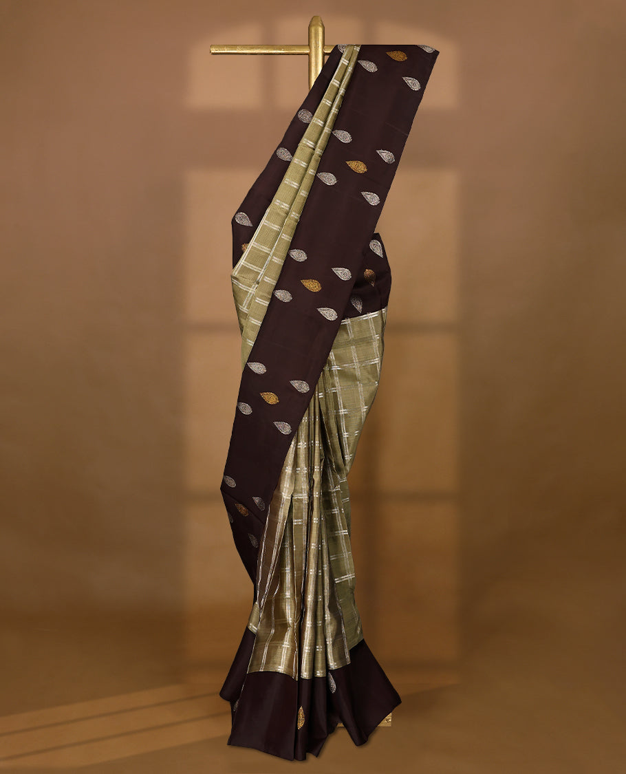 Pastel olive Colour traditional Kancheepuram silk saree adorned with antique check patterns on the body, featuring a deep brown simple border with paisley motifs, and paired with a matching blouse.