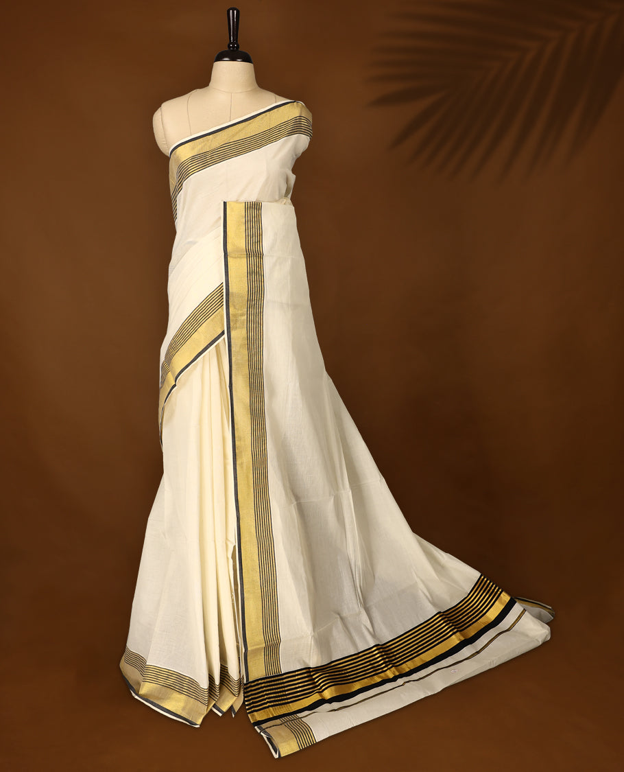 Classic pure cotton Kerala saree with a cream base, golden zari border, and elegant black striped detailing, A timeless choice for traditional events and festive occasions & Comes with a matching blouse piece.