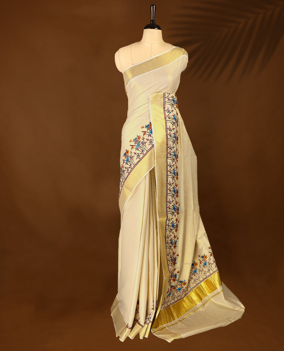 Light Gold colour Tissue Kerala saree featuring Plain body and a beautifully woven Gold Kasavu border with Heavy Blue and mustard colour Floral embroidery work, paired with a matching blouse perfect for festive occasions.