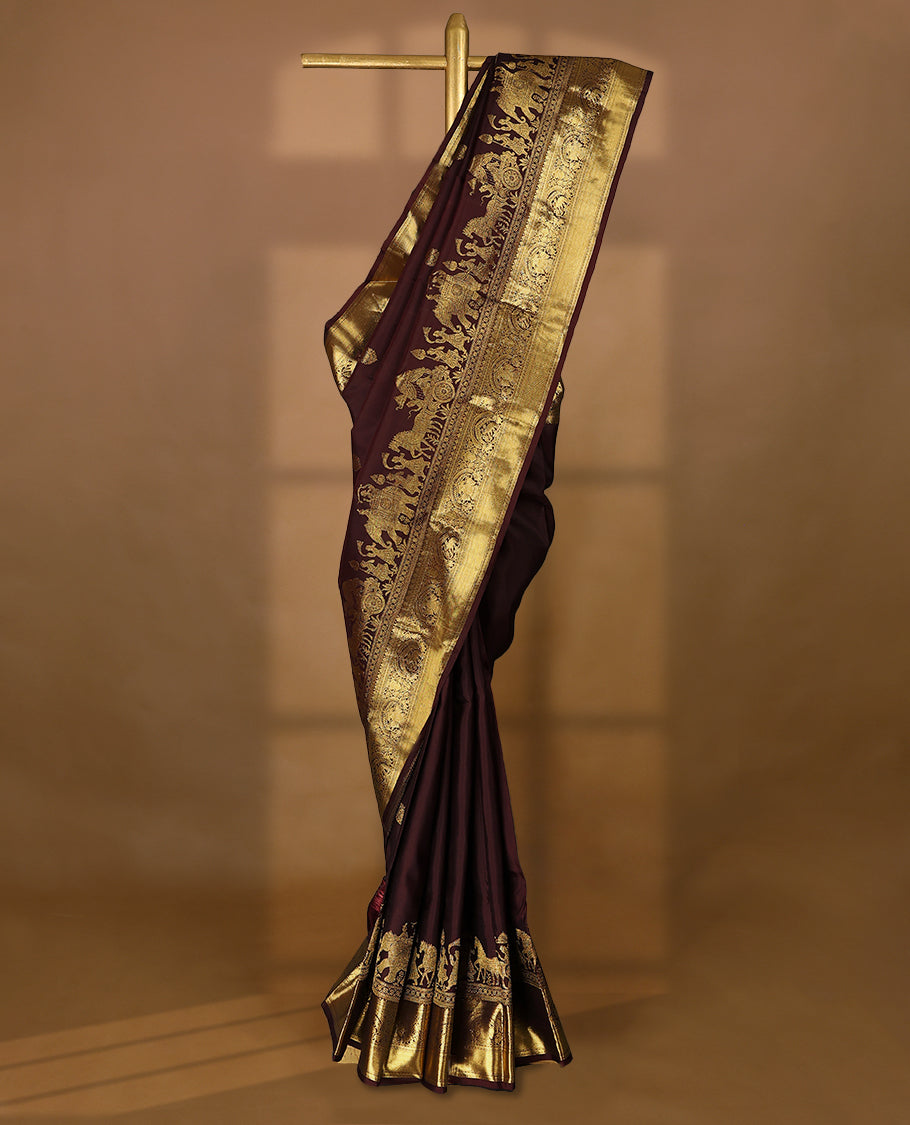 Dark brown colour pure traditional Kancheepuram silk saree adorned with golden Floral motifs on the body, featuring an exquisite antique zari border, paired with a contrasting blouse.