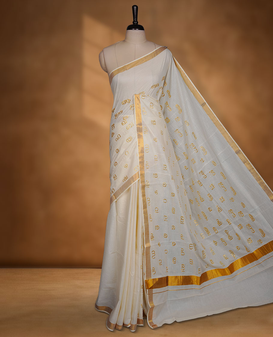 Off-white colour cotton Kerala saree, featuring a classic gold kasavu border and delicate gold-toned Malayalam script motifs woven across the body and pallu. paired with a matching blouse