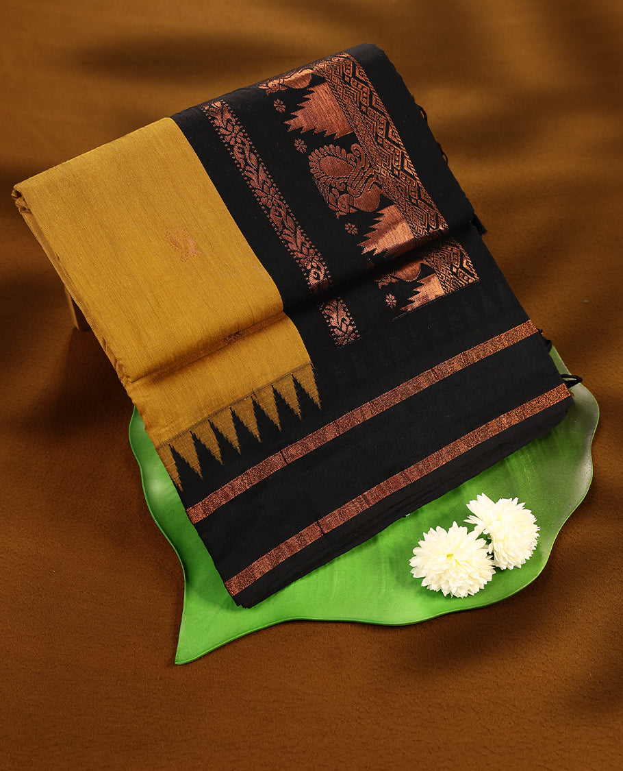 Mustard colour mixed Kalyani cotton saree featuring gold zari motifs throughout the body, paired with a Black colour traditional border and pallu, with matching blouse