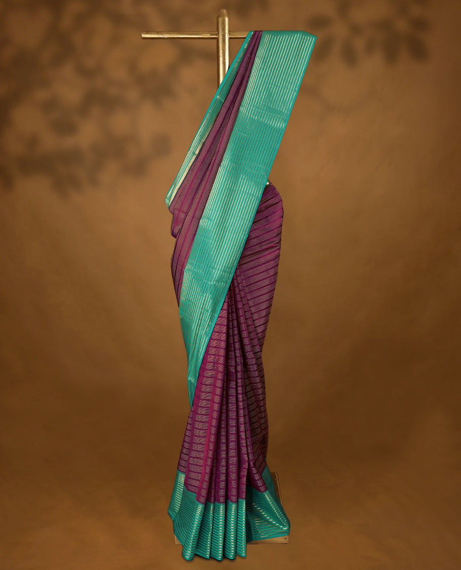 Grape coloured soft silk saree, adorned with golden zari stripes across the body, paired with a contrasting aqua-coloured border embellished with intricate golden zari work, paired with a matching contrast blouse