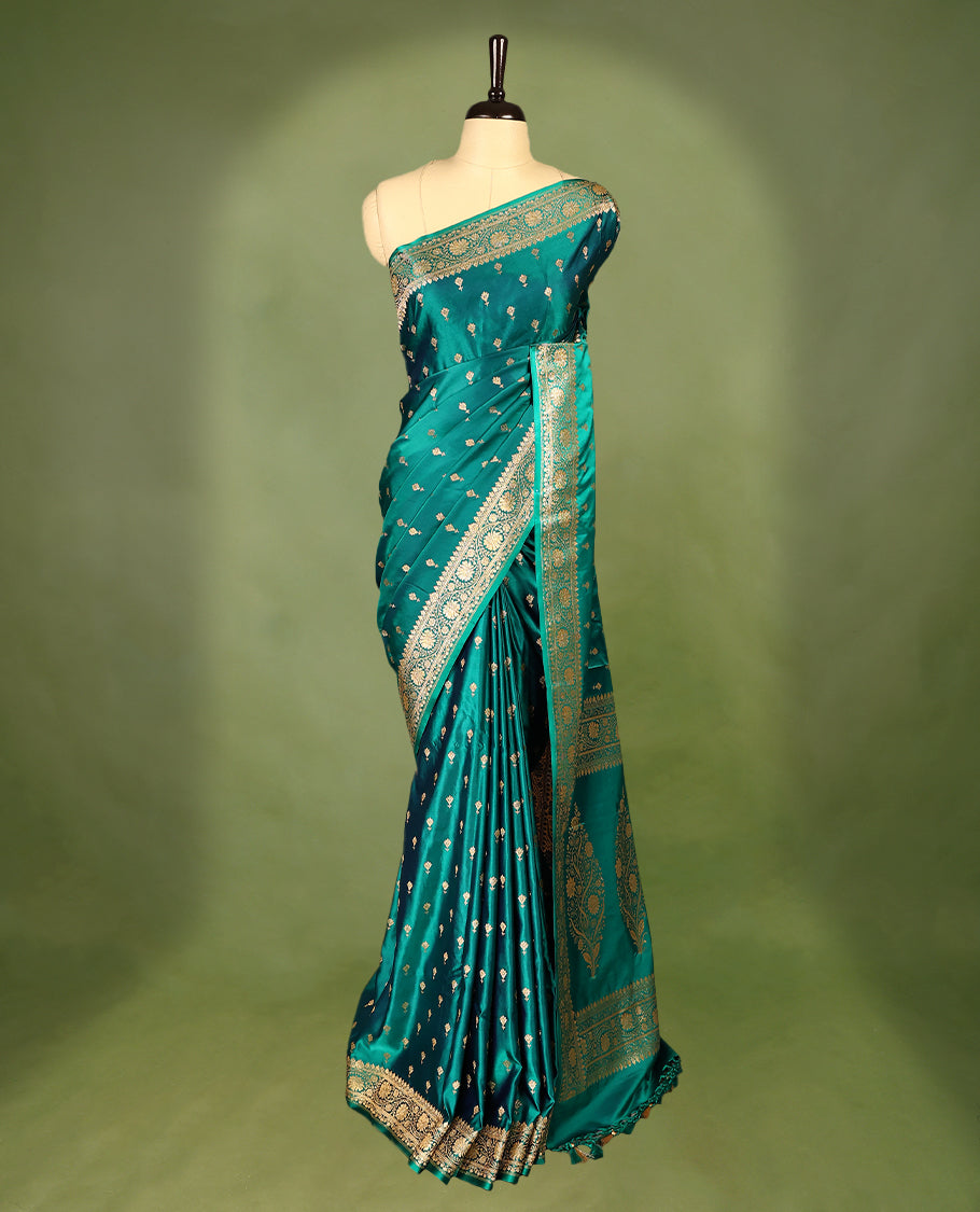 Deep sea green colour semi Banaras satin crepe saree featuring gold zari woven flower motifs across the body, complemented by an intricately designed traditional banarasi border and richly woven pallu, paired with a matching blouse piece.