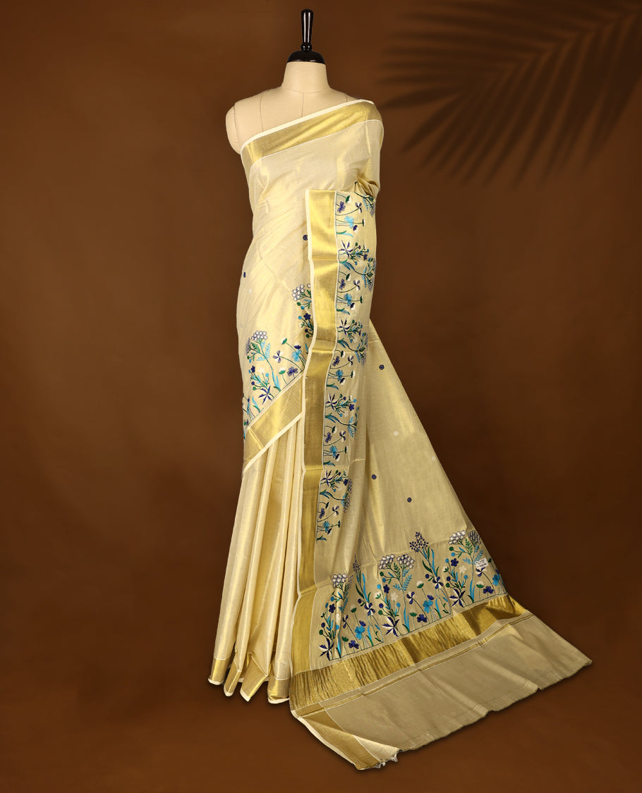 Light Gold colour Tissue Kerala saree featuring Blue and white Colour Floral thread work on body and a beautifully woven Gold Kasavu border, paired with a matching blouse perfect for festive occasions.