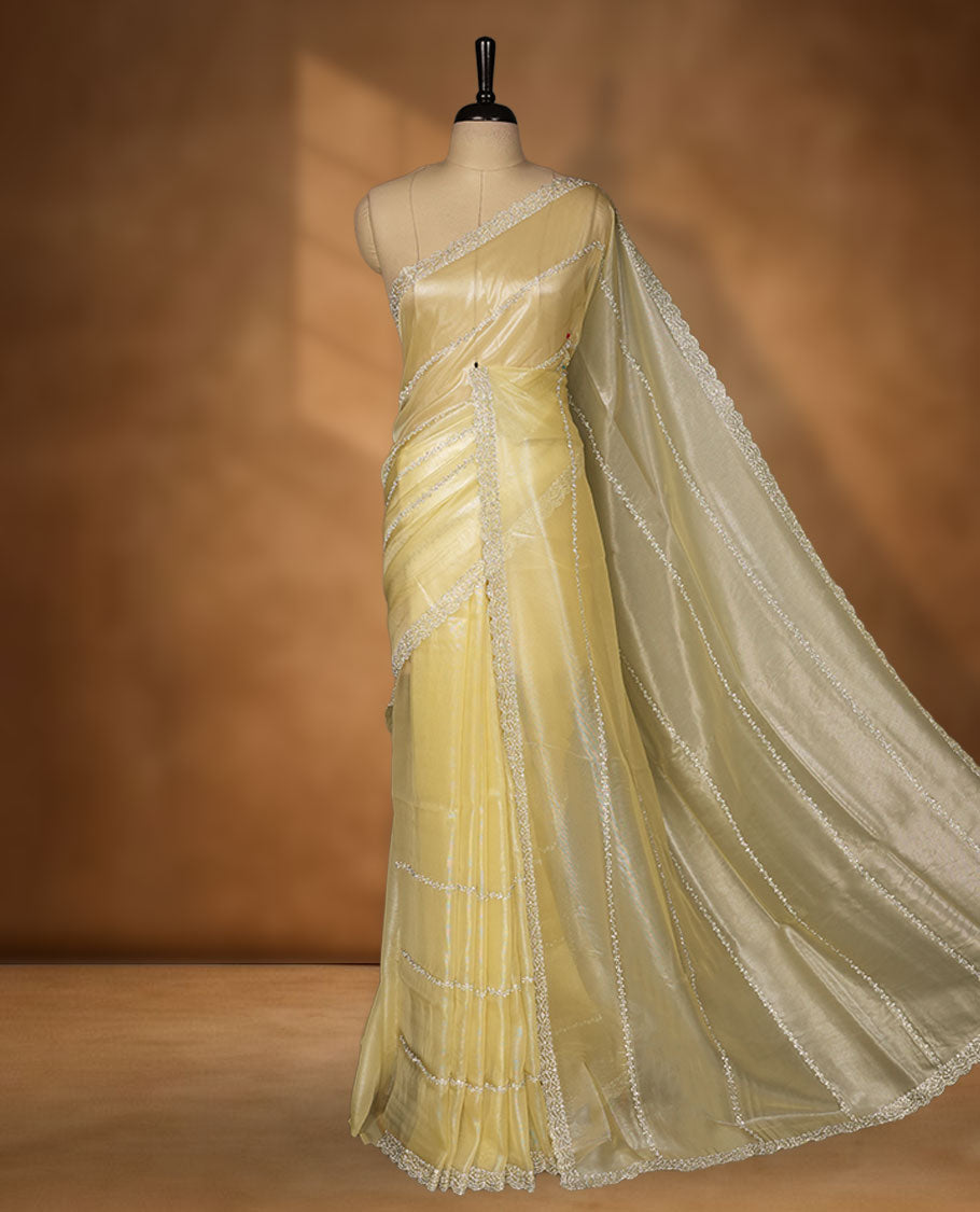 Pale yellow colour net shimmer fancy saree adorned with scattered white stone buttas all over the body, paired with a delicate stone worked border and matching blouse.