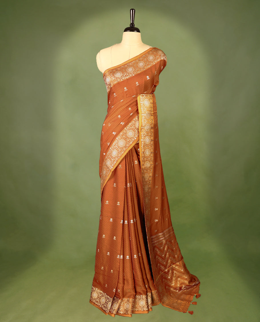 Burnt orange colour pure Banaras crepe saree showcases elegant silver zari Flower Motifs all over the body, a traditional Banarasi gold zari border, a rich intricately woven pallu, and comes with a matching blouse.