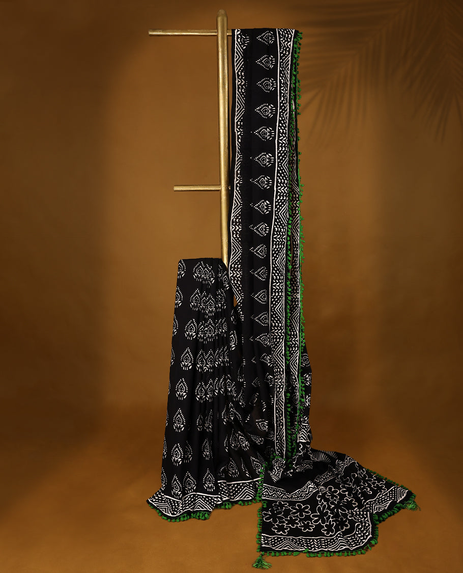 Black cotton saree features intricate white handblock prints, a beautifully detailed border with Green piping and Self Coloured Blouse