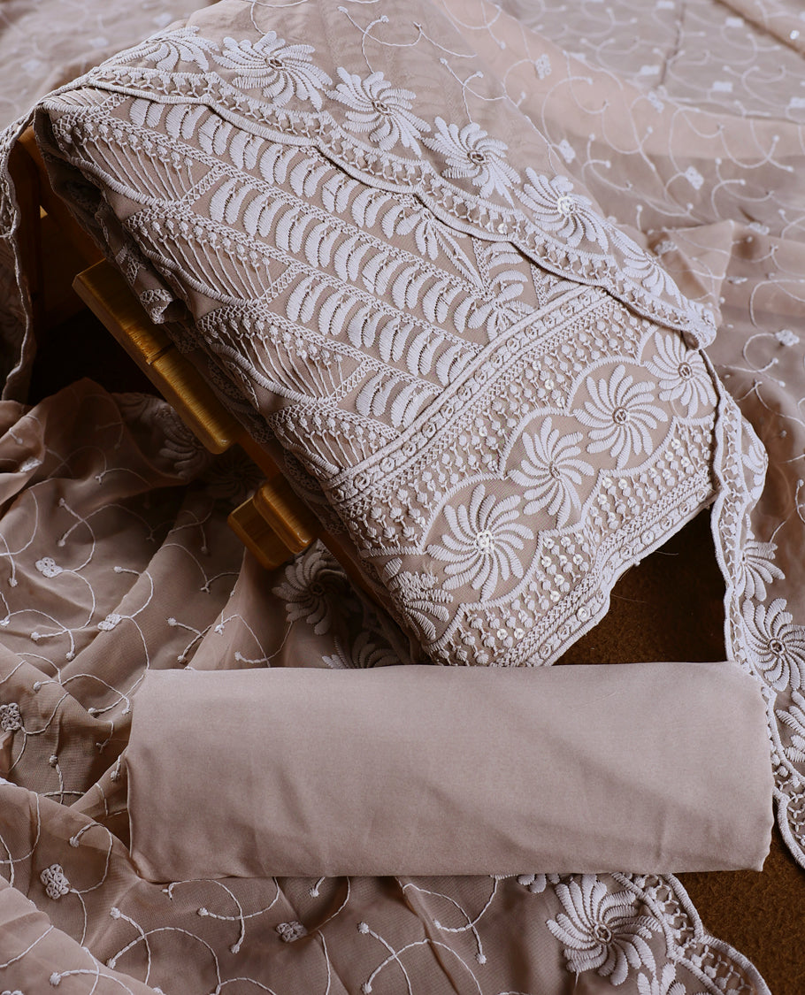 Graceful Taupe colour churidhar material adorned with intricate white floral embroidery and delicate thread patterns, paired with a plain matching bottom and embroidered dupatta, perfect for festive and elegant occasions