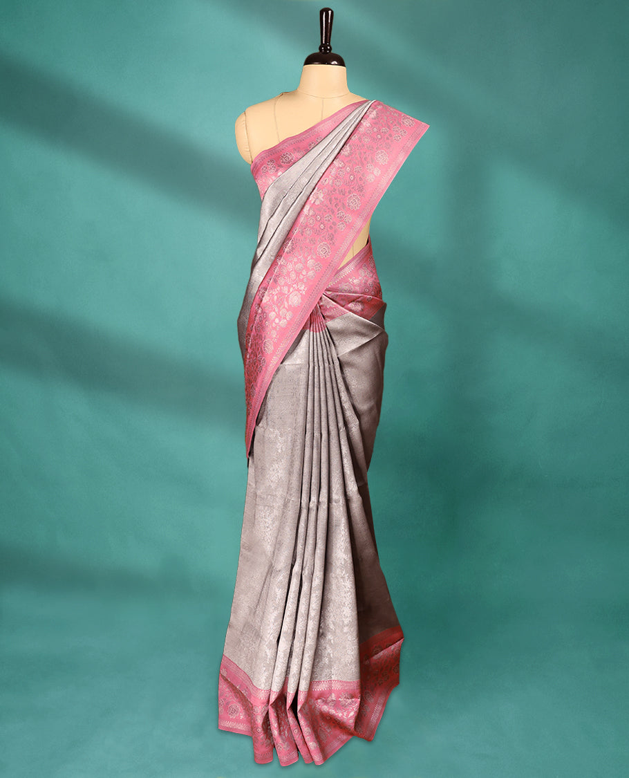 Silver coloured semi silk saree featuring a self coloured floral jaal design on the body, paired with an onion coloured border and matching blouse.