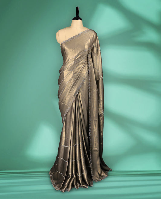 Khaki Beige colour shimmer fancy saree adorned with subtle horizontal Gold stone patterns on the body, paired with a delicate stone worked border, with matching blouse