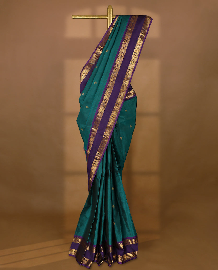 Deep teal blue Colour pure Kancheepuram silk saree with small peacock and elephant motifs, featuring a deep purple border with arched floral and paisley gold zari patterns, paired with a matching blouse.