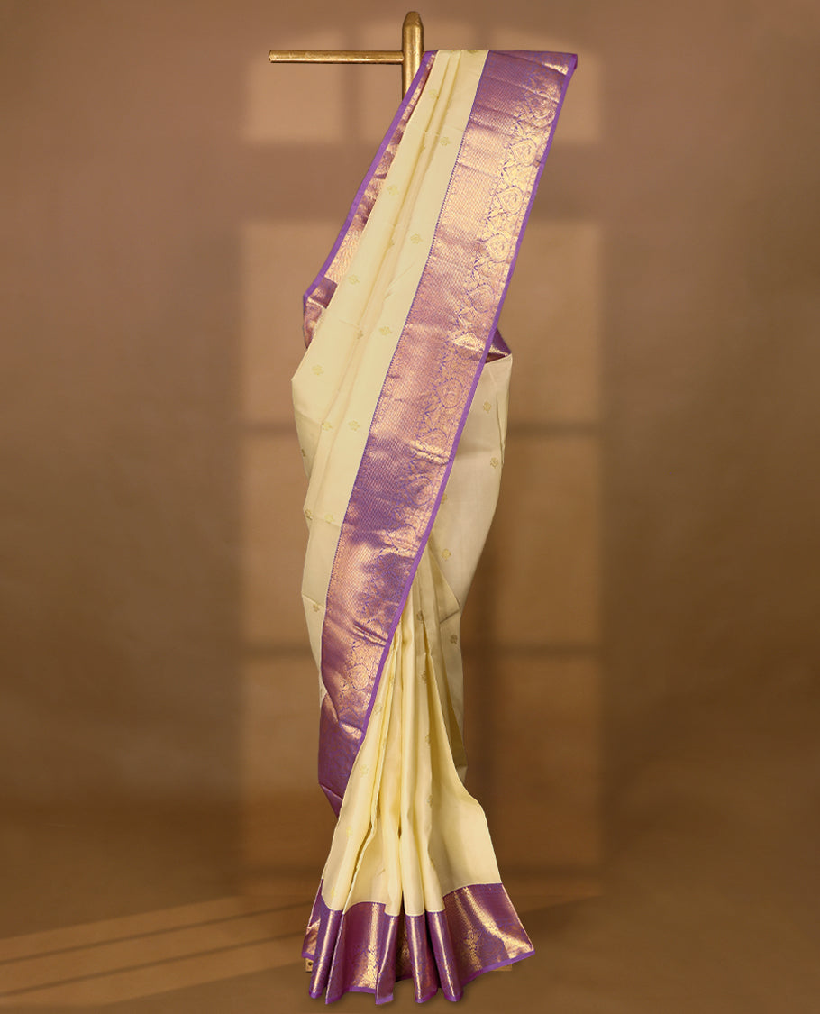 Cream Colour traditional Kancheepuram silk saree adorned with golden motifs on the body, featuring a Light Purple traditional border with Rudraksham and mango designs, paired with a matching blouse.