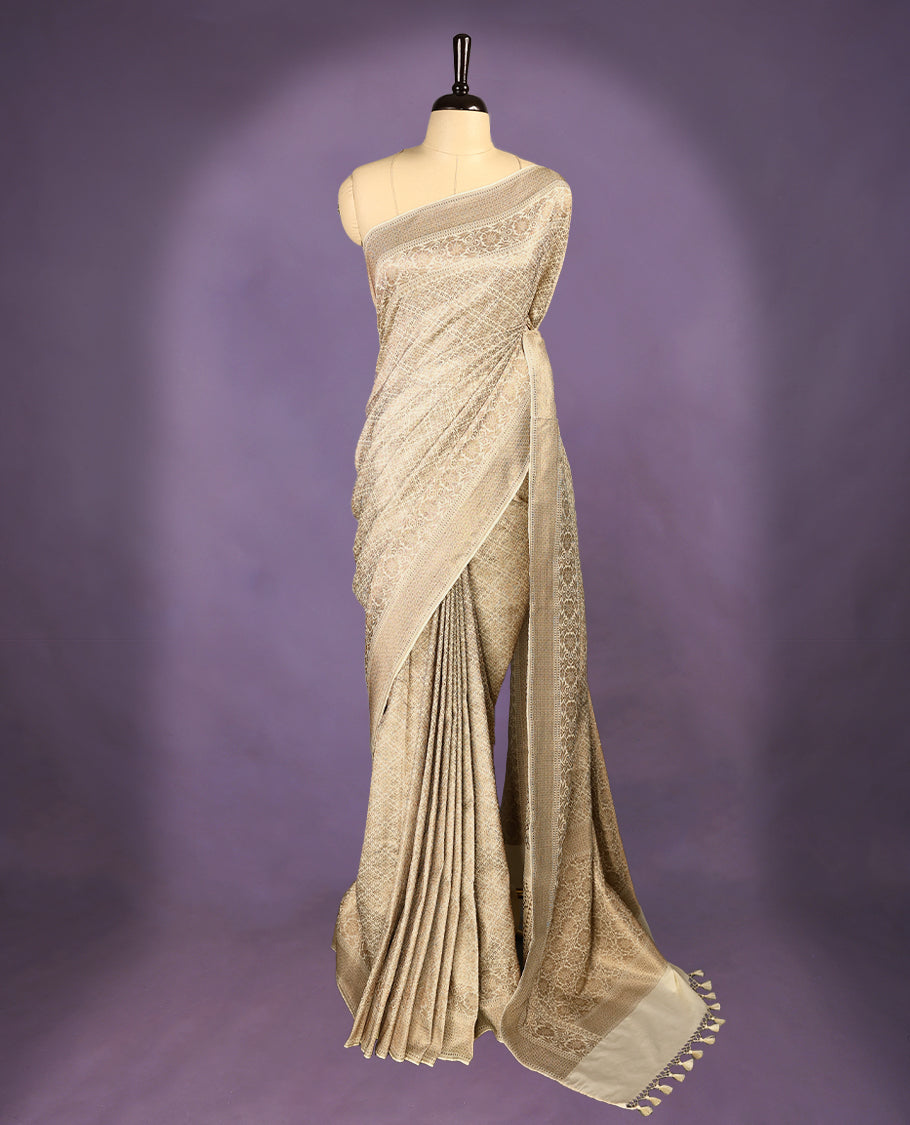 Off White colour semi Banaras Katan saree featuring an antique Gold zari jacquard body, complemented by a self colour traditional border with a floral kodi design, paired with a matching blouse