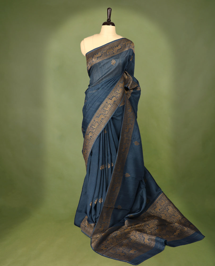 German Blue semi-Banaras tussar georgette saree adorned with antique zari butta motifs on the body, accentuated by a beautifully crafted jungle-themed border, and paired with a matching blouse.