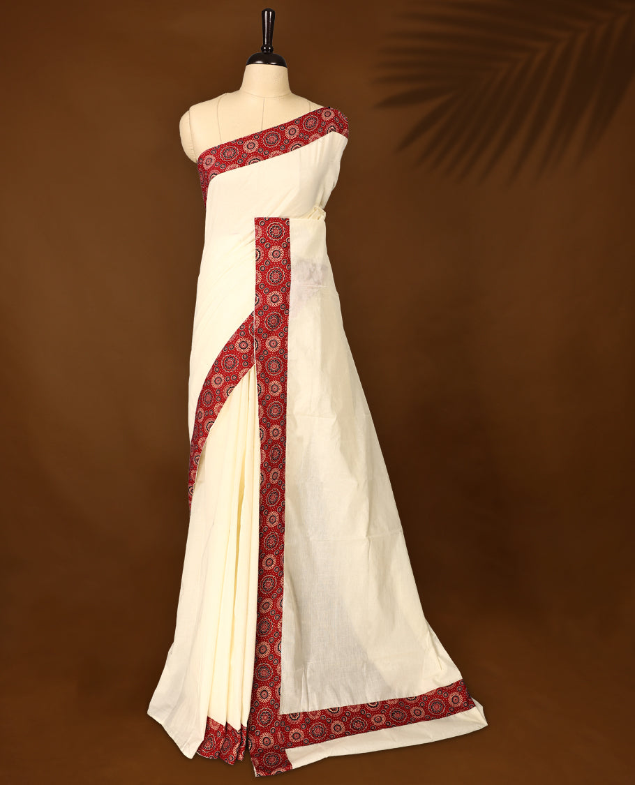 off white saree with a striking red printed border. The border features circular floral motifs in black and cream, with dotted detailing radiating outward, creating a traditional yet vibrant design