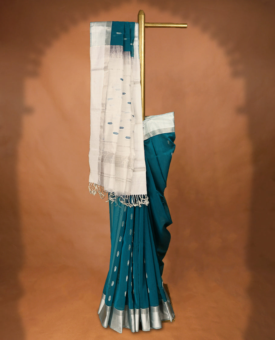 Peacock Blue coloured Maheshwari Cotton saree featuring Silver Zari motifs across the entire body, complemented by a traditional White coloured border and a matching blouse.