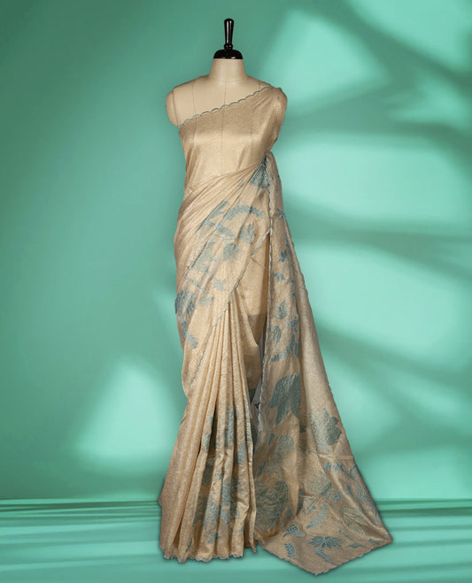 Champagne beige colour organza designer saree featuring subtle woven texture on the body, adorned with soft Blue floral embroidery along the border and pallu, finished with scalloped Thread edging paired with matching blouse.
