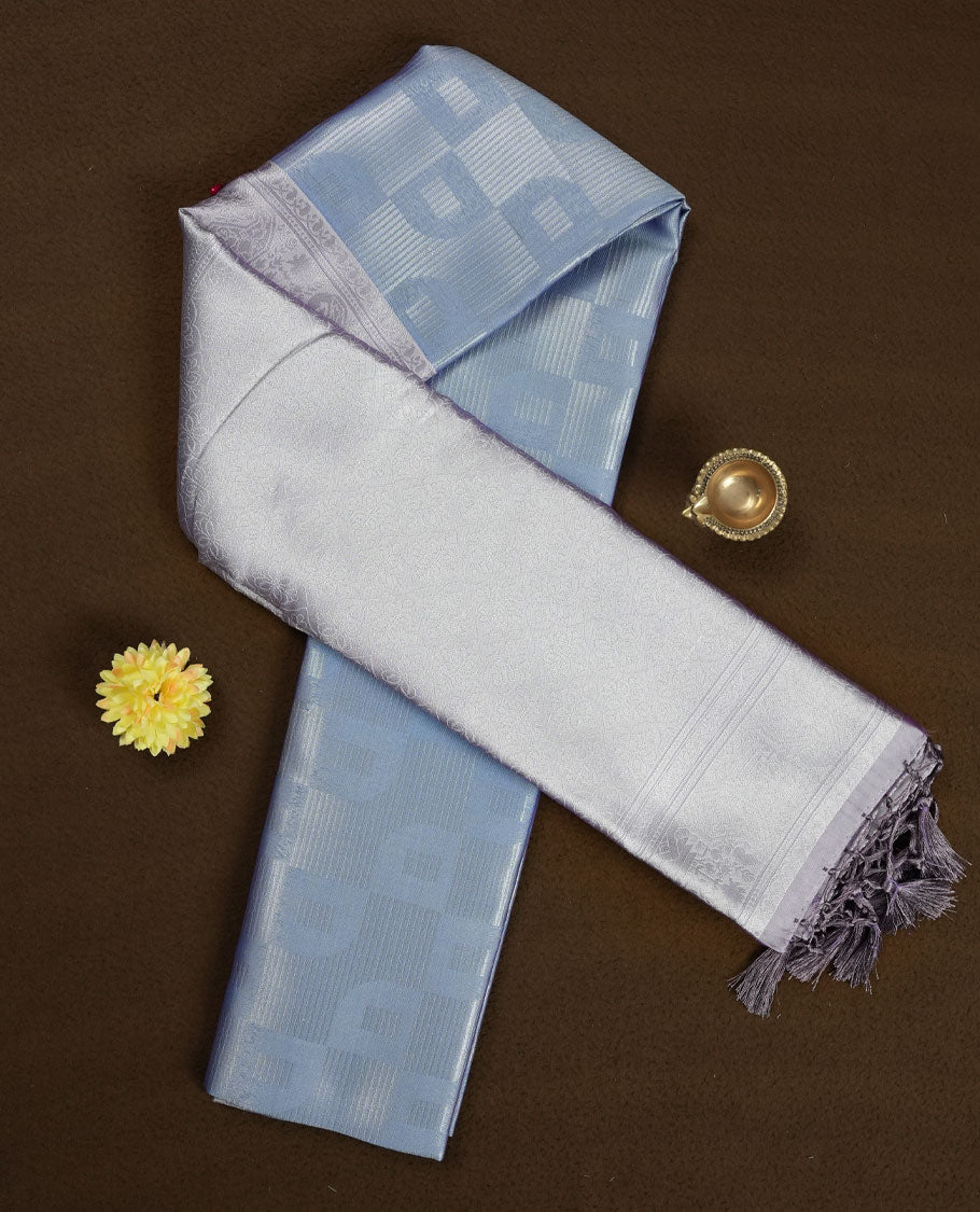 Light lavender colour semi silk saree adorned with subtle silver zari motifs on the body, complemented by a pastel light blue pallu intricately woven with rich floral patterns border and pallu, and paired with a matching blouse