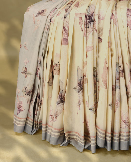 Cream colour semi silk printed saree adorned with pastel onion floral motifs across the body, finished with a light Blue and light Brown striped border, with matching blouse