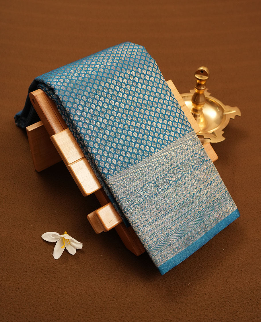 Teal colour semi silk brocade saree featuring intricate Gold patterns across the body, complemented by a Self colour woven border and pallu, paired with a matching blouse.