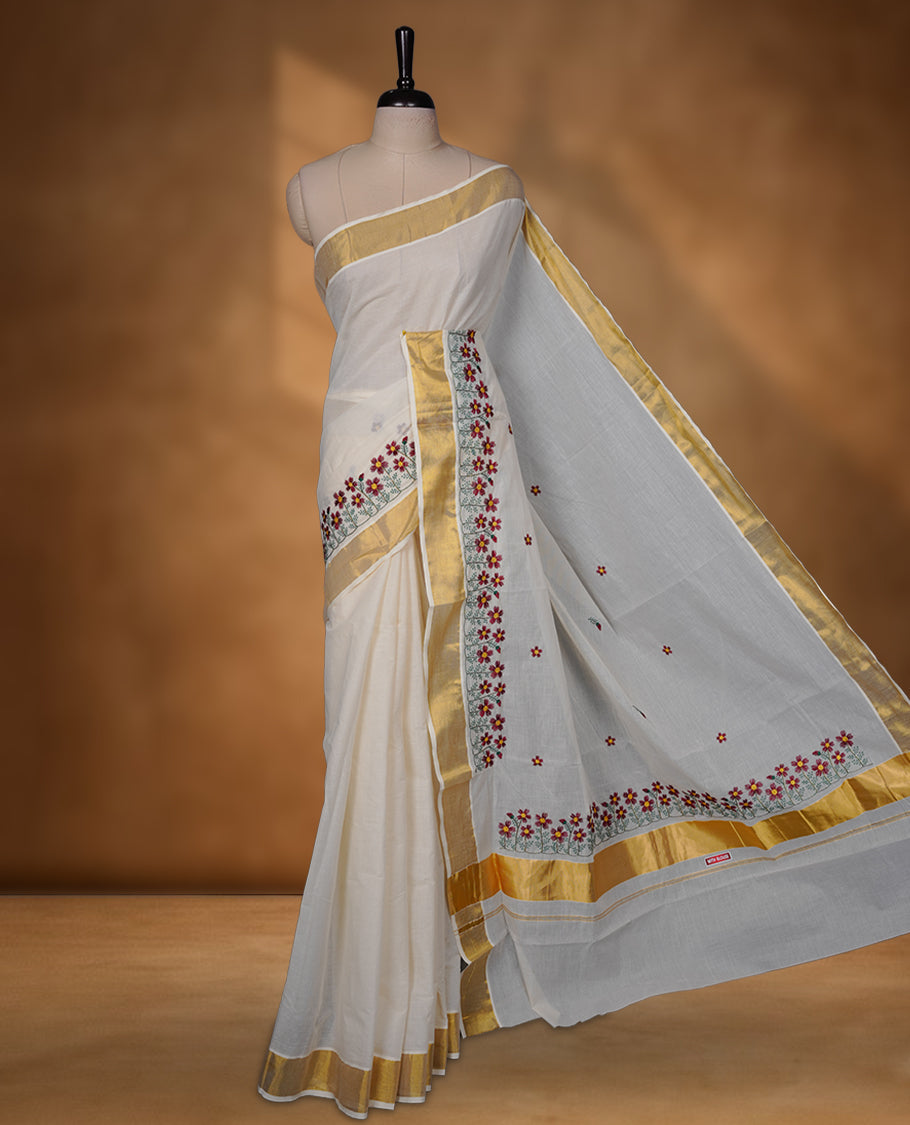 Off-white colour Kerala saree with a classic gold kasavu border, delicately embroidered floral motifs in red and green across the body and pallu, finished with a subtle golden sheen for timeless elegance.