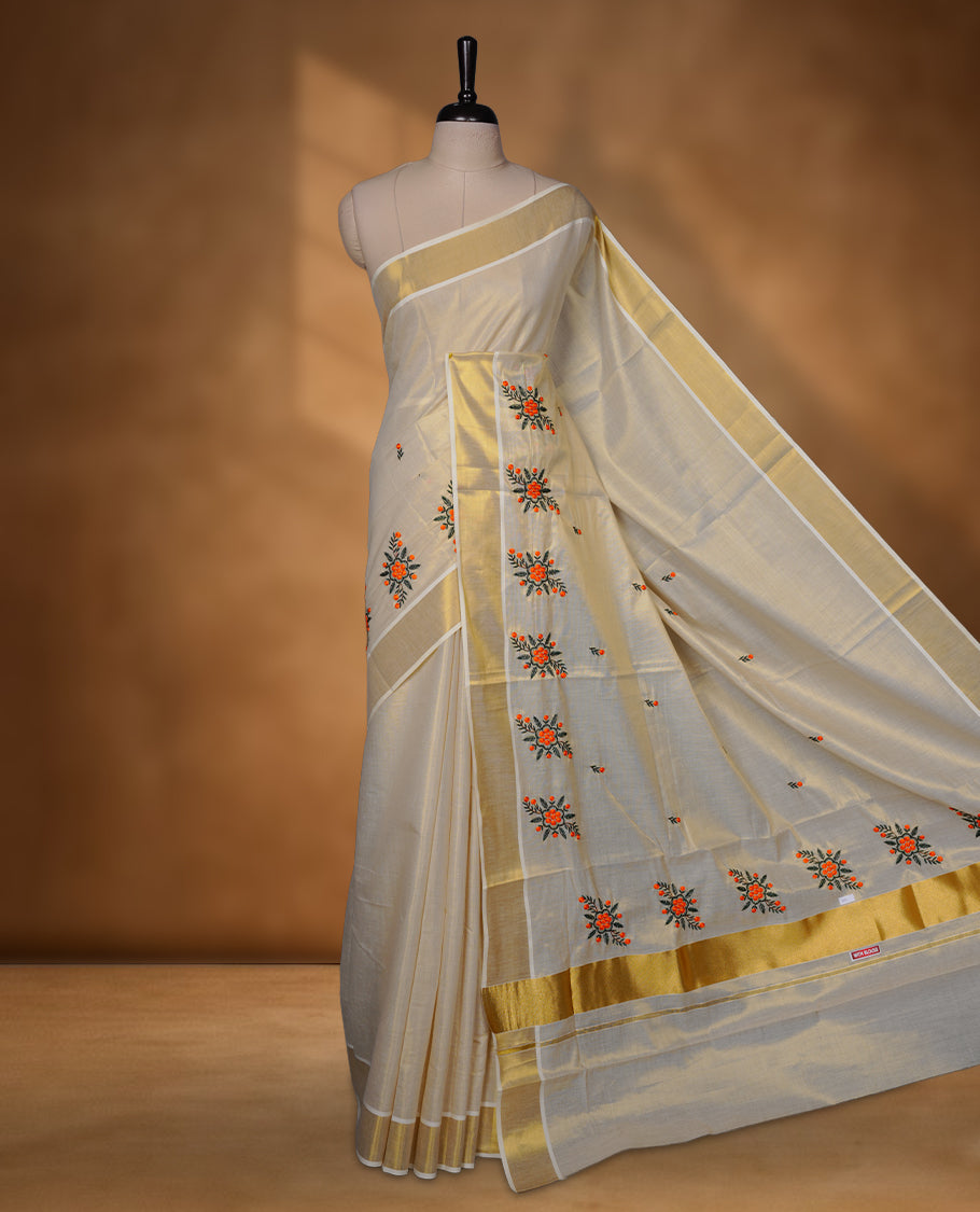 Off-white colour tissue Kerala saree with a classic gold kasavu border, highlighted by delicate orange floral embroidery across the body and pallu, and paired with a matching blouse.