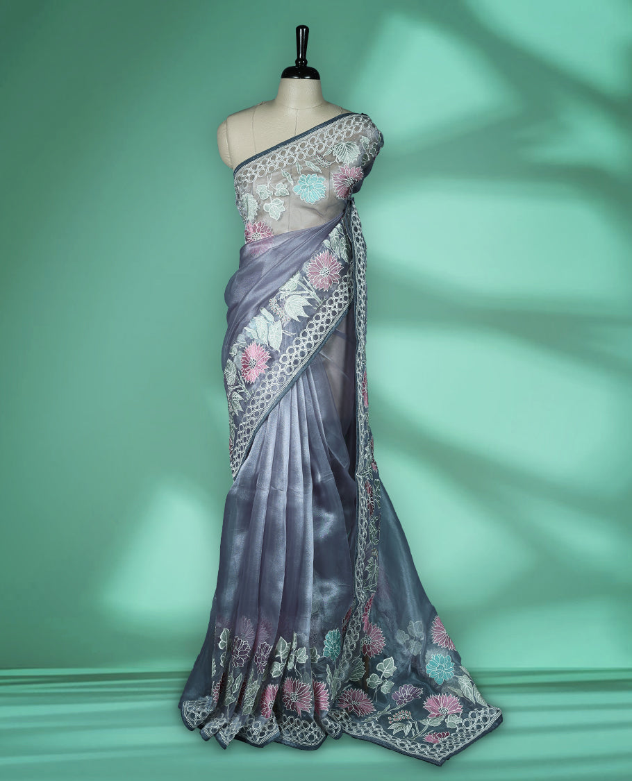 Grey colour organza designer saree featuring delicate pastel floral embroidery in pink, mint green, and white across the body, with a scalloped border accentuated by floral threadwork, and a gracefully embroidered pallu paired with matching blouse.