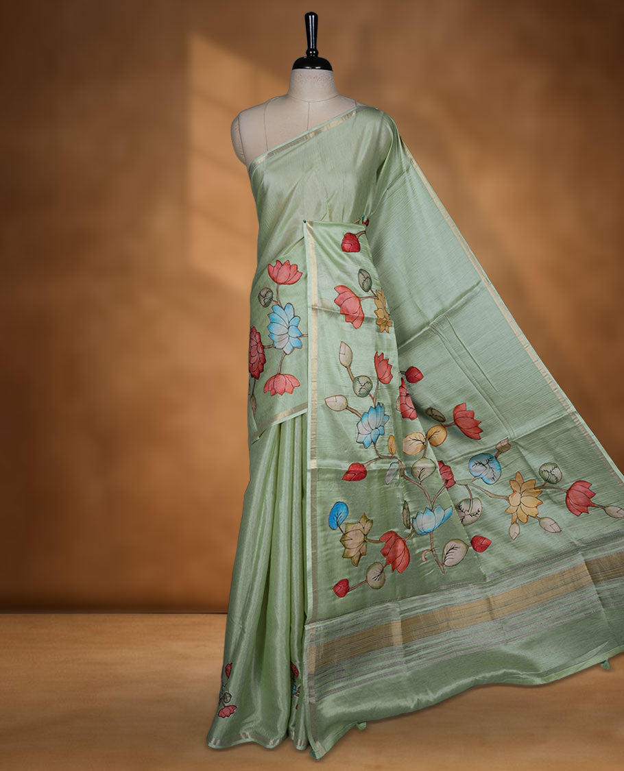 pastel green semi tusser silk saree featuring hand painted floral motifs across the pallu and lower body, highlighted with a subtle zari border and paired with a matching blouse.