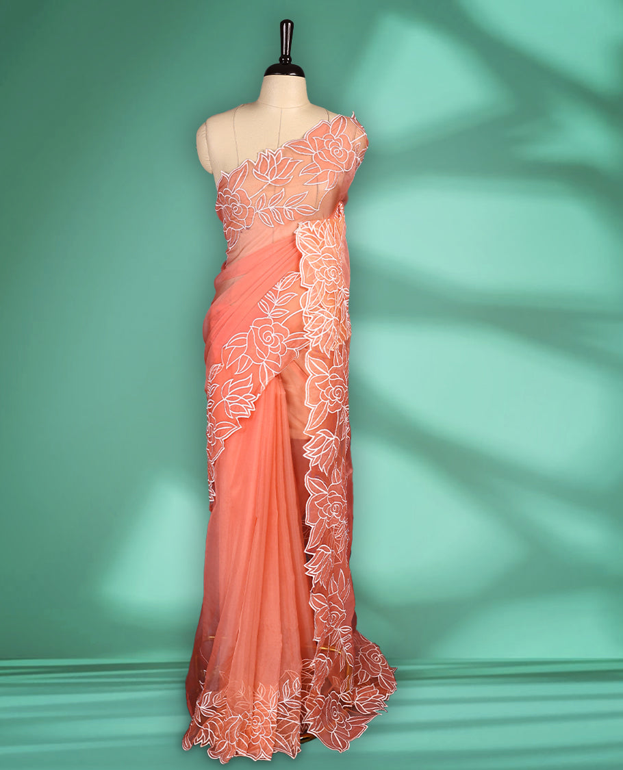 Peach colour net organza exclusive designer saree featuring a plain body and a beautifully adorned border with applique and thread embroidery work, complemented by a rich pallu and paired with a matching blouse