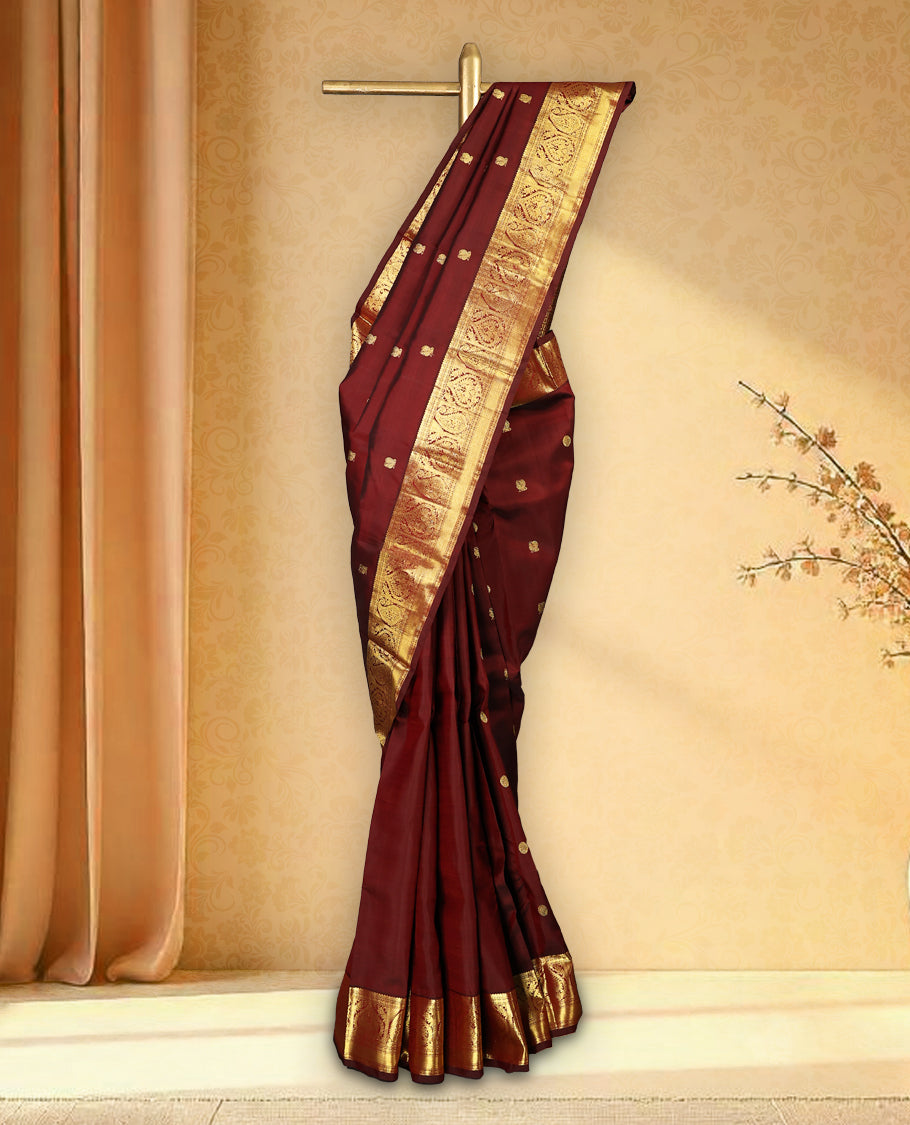 Deep maroon colour pure Kancheepuram traditional saree featuring gold zari Mayoora Chakra motifs across the body, enhanced with a classic traditional border with Peacock and mango design and a grand pallu with Mango designs, paired with a matching blouse.