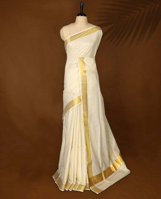 Elegant off white colour cotton Kerala saree with fine checkered patterns and a lustrous golden zari border, Paired with a matching blouse, it’s perfect for traditional functions and festive wear.
