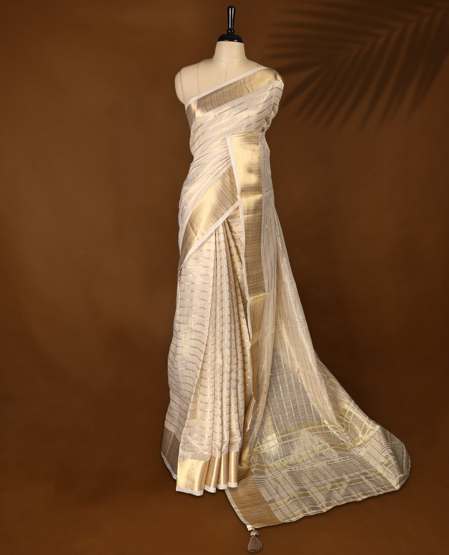 White & gold colour Organza Kerala saree featuring a smooth body with Gold zari Stripes, highlighted by a sleek golden zari border, Bold pallu Paired with a matching blouse.