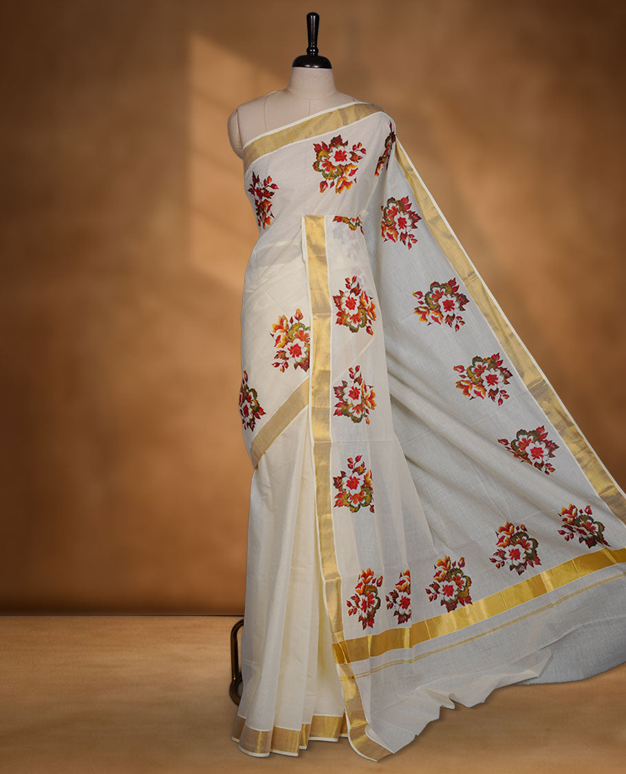 Off-white colour cotton Kerala saree with a classic gold kasavu border, adorned with multicolour floral motifs across the body and pallu, and paired with a matching blouse.