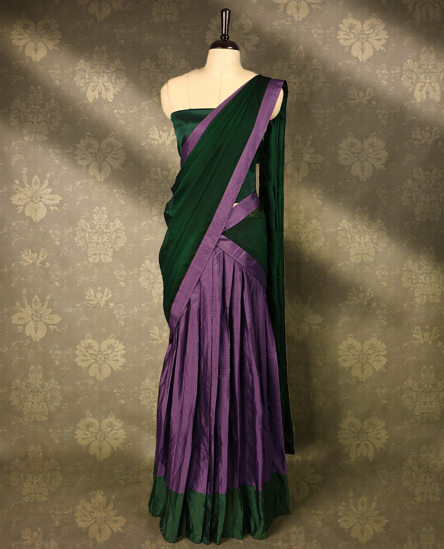 Lavender colour semi-stitched traditional half saree in semi Banarasi silk, featuring a checked design with a Bottle Green bordered skirt. It is paired with a Rangoli georgette drape and comes with a blouse that matches the skirt’s border.