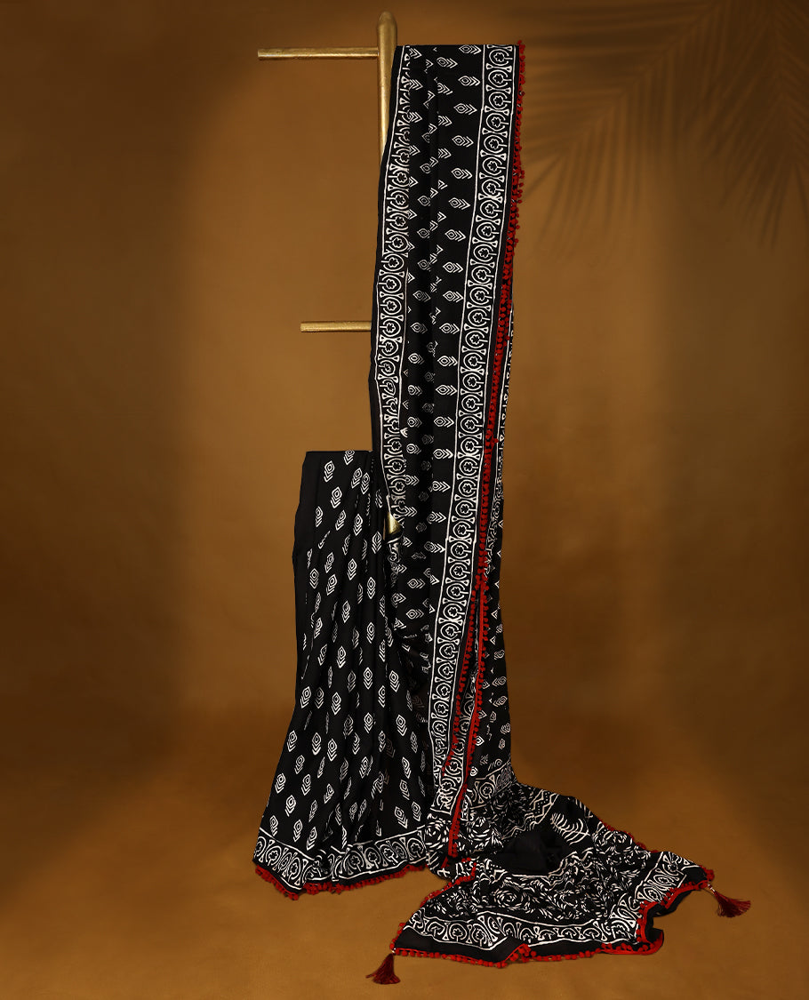 Black cotton saree features intricate white handblock prints, a beautifully detailed border with red piping and Self Coloured Blouse