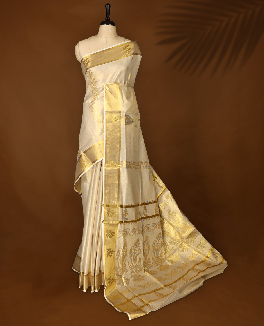 Elegant off white colour tissue Kerala saree featuring rich golden floral motifs and a shimmering zari border, exuding traditional charm and grace, Comes with a matching blouse to complete the timeless look.