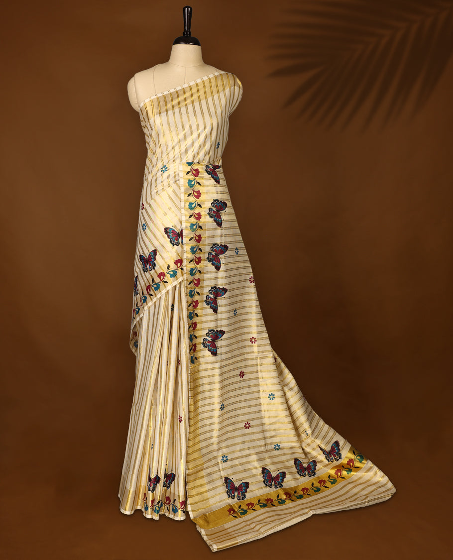 Elegant off white Kerala tissue saree with golden stripes, adorned with multicolor butterfly and floral motifs, and finished with a rich golden zari border with kodi prints perfect for a festive, graceful look with matching blouse.