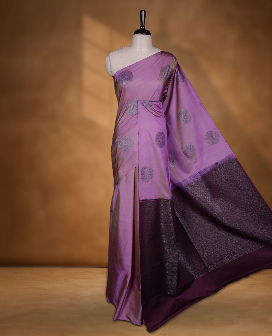 Lavender colour semi soft silk saree adorned with delicate woven floral chakkram motifs on the body, complemented by a contrast purple colour woven pallu with intricate detailing and tassel accents without border & Comes with a matching blouse piece.