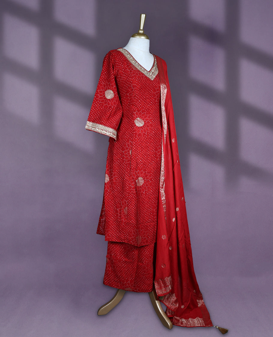 Deep red colour salwar set with V neck and elbow sleeves featuring bandhani inspired dotted pattern with gold motifs paired with matching bottom and dupatta with tassel detail